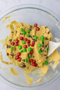 A glass bowl full of chocolate chip cookie dough, red and green M&Ms have been added