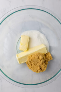 A glass mixing bowl with butter, brown sugar, and white sugar in it