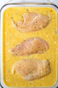 A glass baking pan full of a soup and rice mixture topped with boneless skinless chicken breasts.
