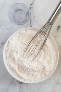 Flour and other dry ingredients in a white bowl with a whisk