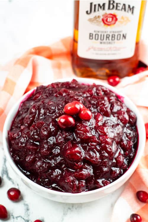 A white bowl with cranberry sauce with a bottle of bourbon in the background
