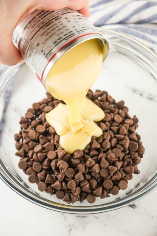 a glass bowl with chocolate chips in it, sweetened condensed milk is being poured on top