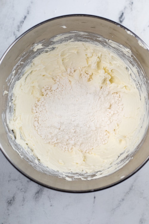 A metal mixing bowl full of creamed cream cheese and dry cake mix.