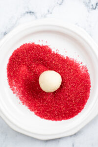 a white dough ball in the center of a white plate covered in red sanding sugar.