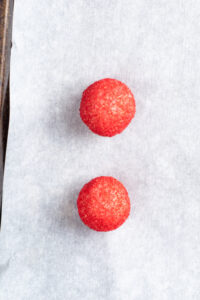 Two red sugar covered dough balls on a parchment lined baking sheet