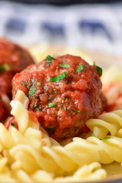 A close up of a meat ball covered in sauce in a bowl of rotini pasta