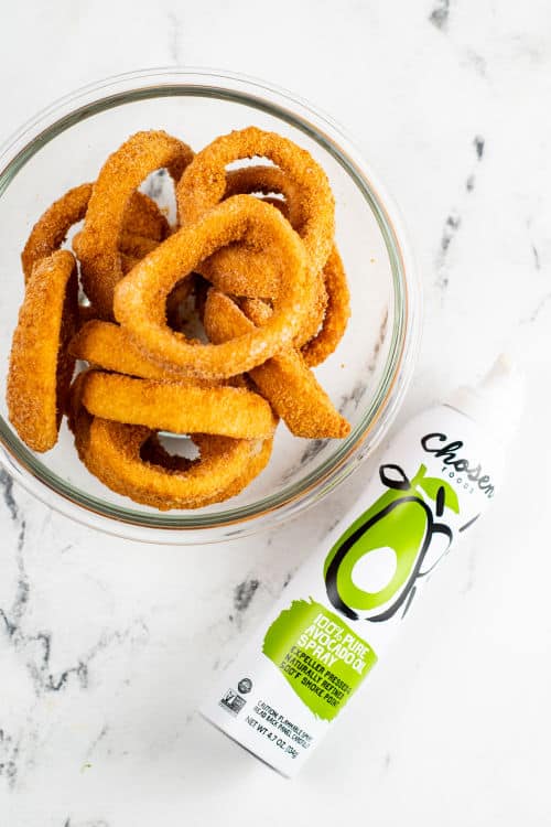 a bowl of frozen onion rings and cooking spray on a white marble background