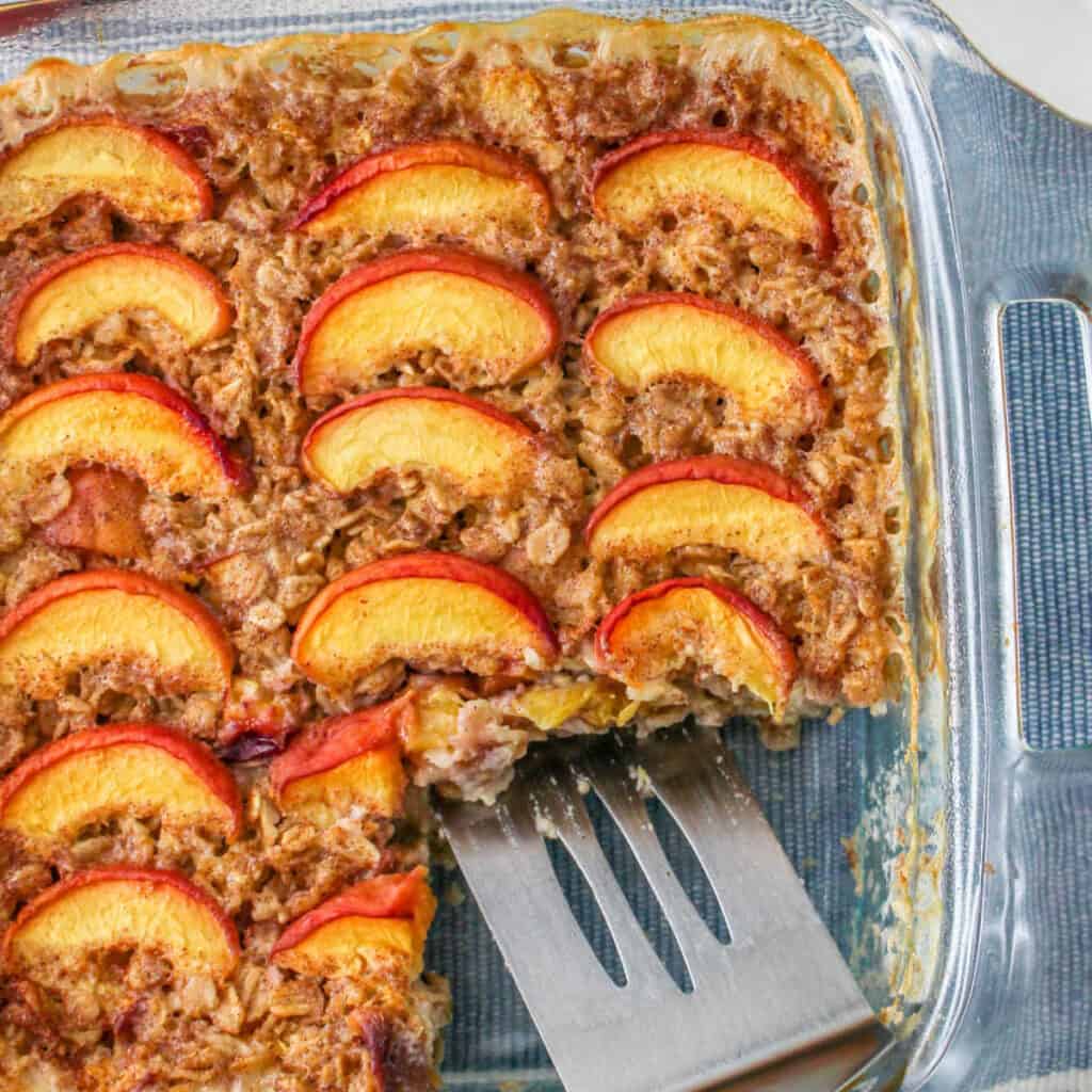 a square baking pan full of peach baked oatmeal, a piece has been removed and there is a spatula in the space.