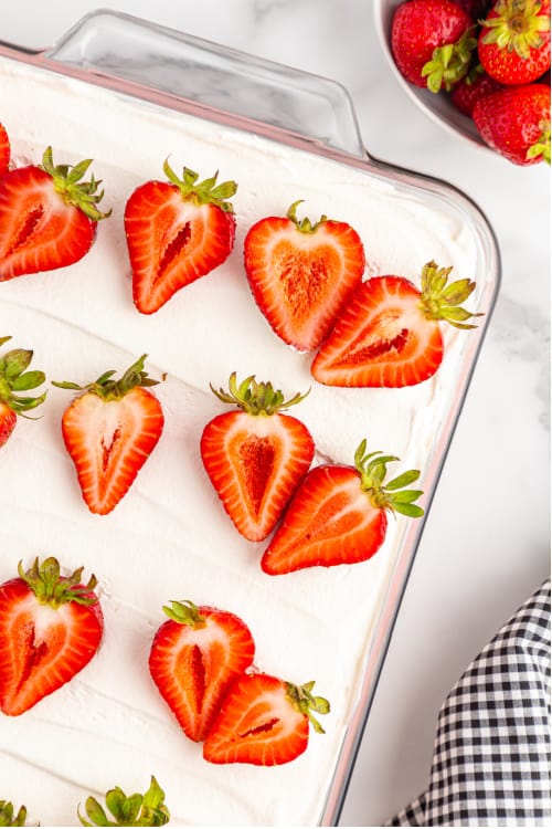 A glass cake pan full of strawberry delight topped with sliced strawberries
