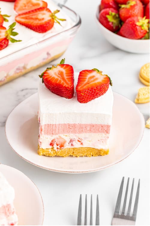A piece of layered strawberry lush on a white plate topped with two slices of strawberries