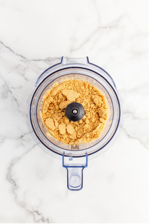 An overhead view of a food processor full of golden Oreo crumbs
