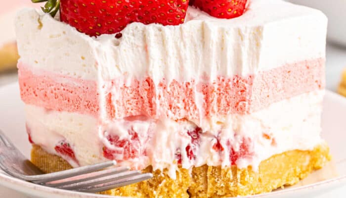 a close up picture of a piece of strawberry delight with a bite taken out showing the strawberry and cream cheese layers
