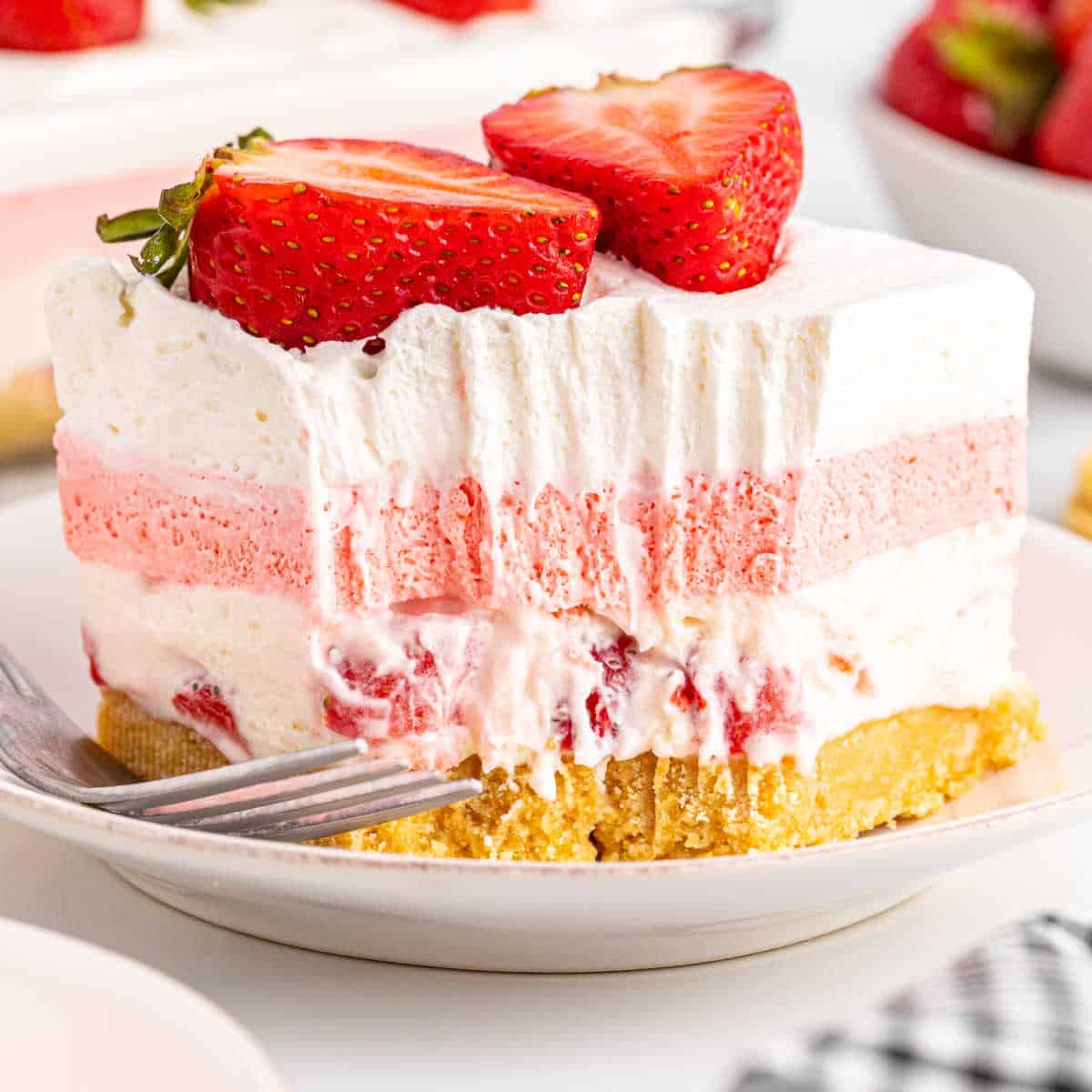 a close up picture of a piece of strawberry delight with a bite taken out showing the strawberry and cream cheese layers