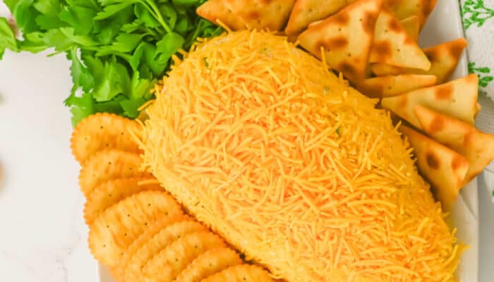An overhead view of a carrot shaped cheese ball on a plate with a variety of crackers